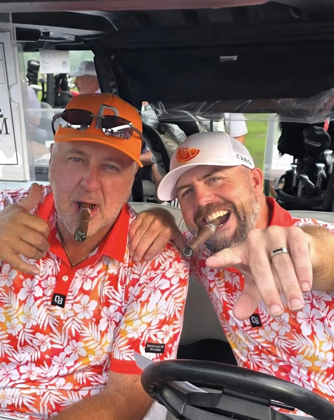 Two golfers sharing a lighthearted cart moment in matching orange floral polos